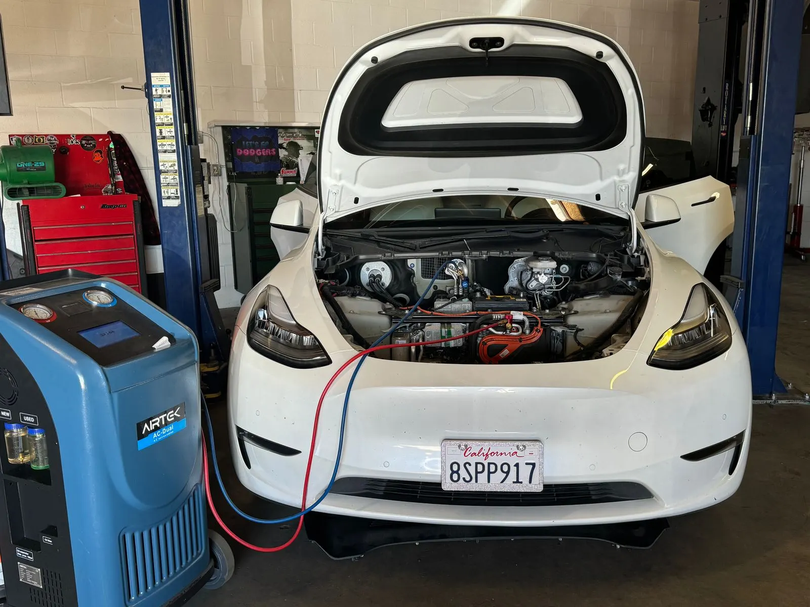 White Tesla Model Y on the lift at Electric City connected to an A/C service machine